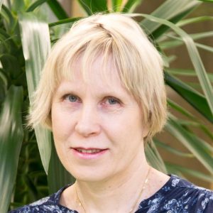 Kuvassa Pirten työterveyslääkäri Taina Harjumaaskola, jolla on lyhyet vaaleat hiukset, tumma pusero ja taustallaan viherkasvi.