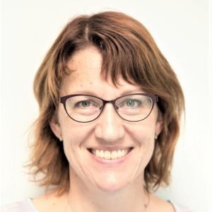 Kuvassa hymyilee Pirten työterveyshoitaja Jenni, jolla on ruskeat olkapäille ulottuvat hiukset ja silmälasit.