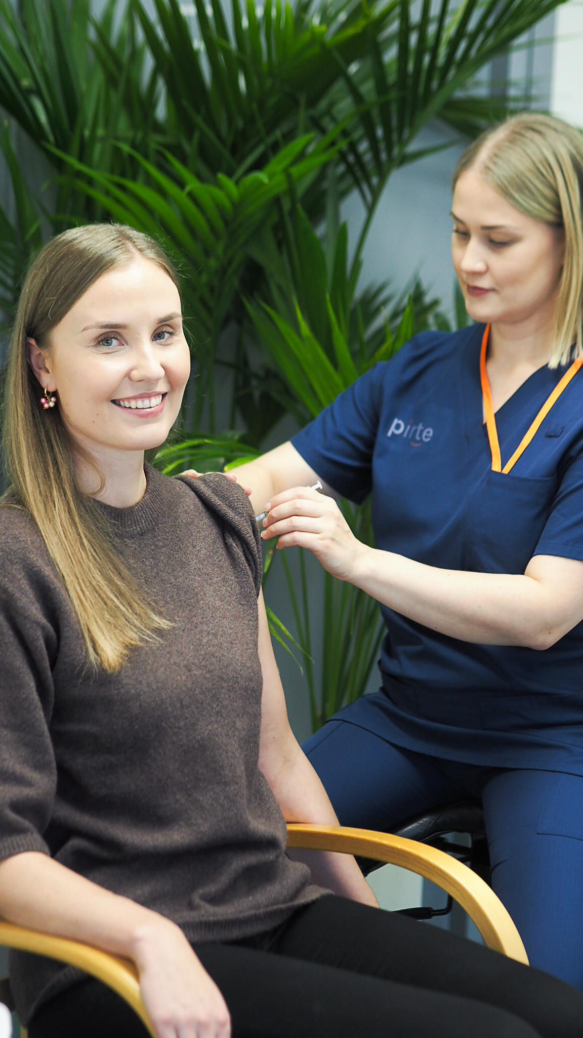 Kuvassa Pirten poliklinikkahoitaja Anni antaa influenssarokotetta pitkähiuksiselle hymyilevälle naiselle. Influenssarokotus antaa hyvää suojaa influenssaa ja sen jälkitautetan vastaan.