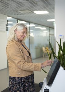 Kuvassa vaaleahiuksinen hymyilevä nainen käyttää Pirte Ratinan ilmoittautumislaitetta.